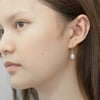 A pair of dangle pearl hook earrings in silver, worn by a woman model