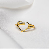 A gold vermeil ring with a heart-shaped design on a white fabric background.