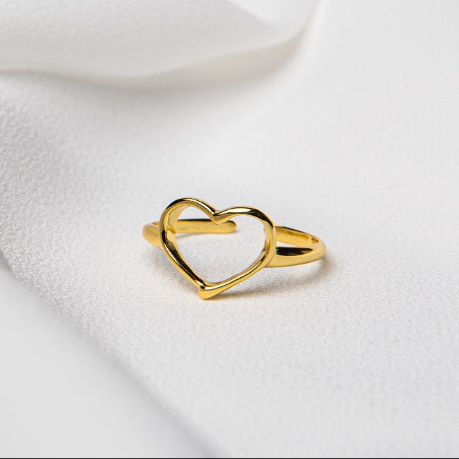 A gold vermeil ring with a heart-shaped design on a white fabric background.