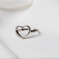A silver ring with a heart-shaped design on a white fabric background.