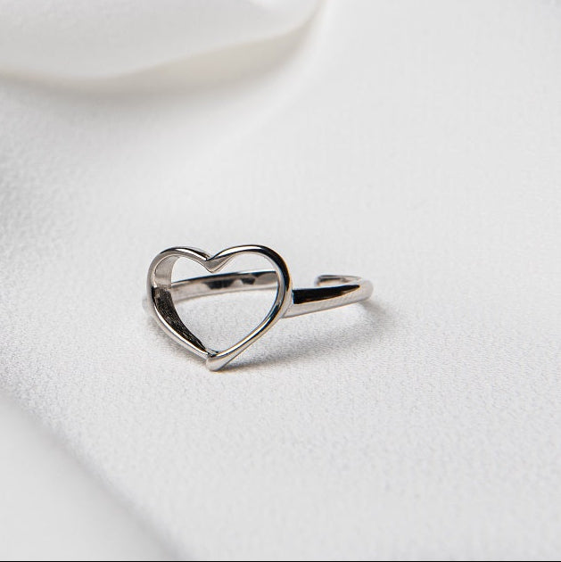 A silver ring with a heart-shaped design on a white fabric background.
