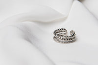 An adjustable sterling silver ring with a twisted design, displayed on a white fabric surface.