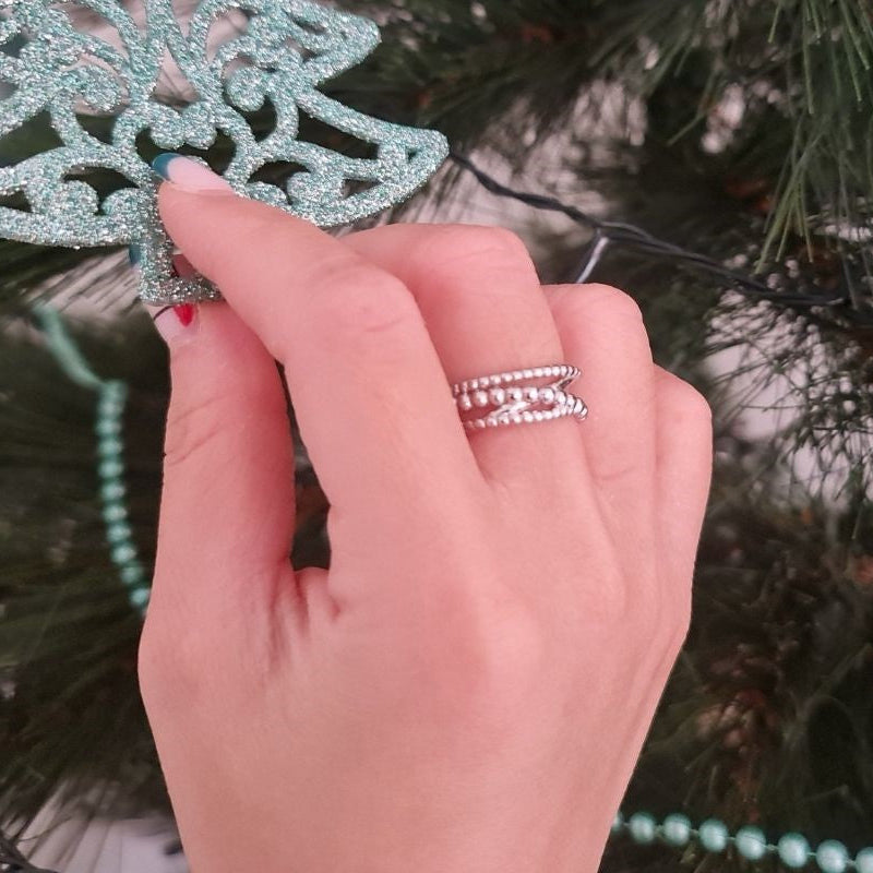 A close up of a womans hand wearing a silver bubble design ring with a christmas background