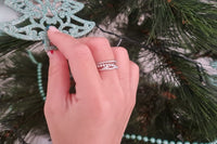 A close up of a womans hand wearing a silver bubble design ring with a christmas background