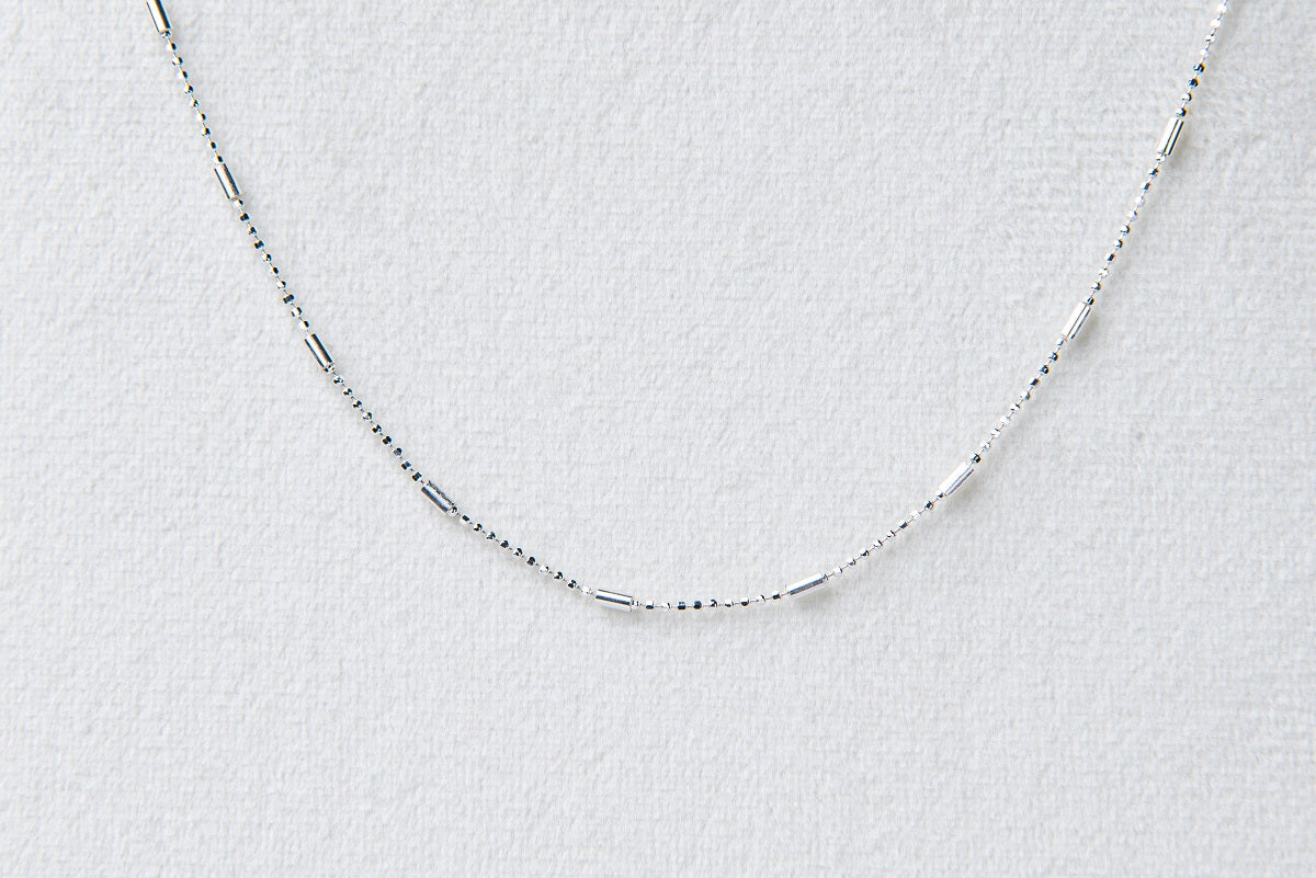 A sterling silver necklace with a series of round beads, laid out on a textured white background.