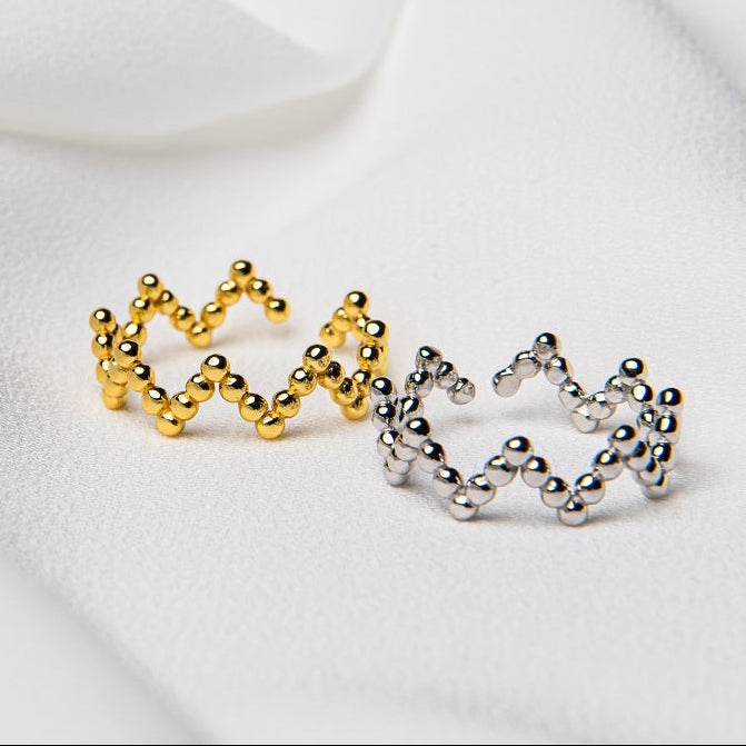 Two rings, one with a gold vermeil finish and the other with a silver finish, both featuring a zigzag design, displayed on a white fabric surface.