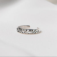 A silver toe ring with wave designs on a white background