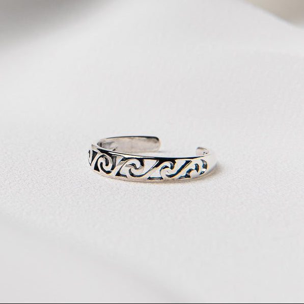 A silver toe ring with wave designs on a white background