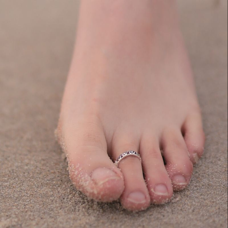 Close up of a foot on the beach wearing a silver toe ring featuring a wave design.