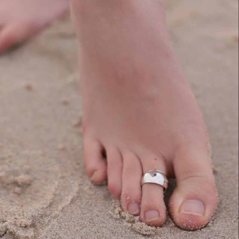 A close up of a foot ont he beach wearing a plain silver toe ring