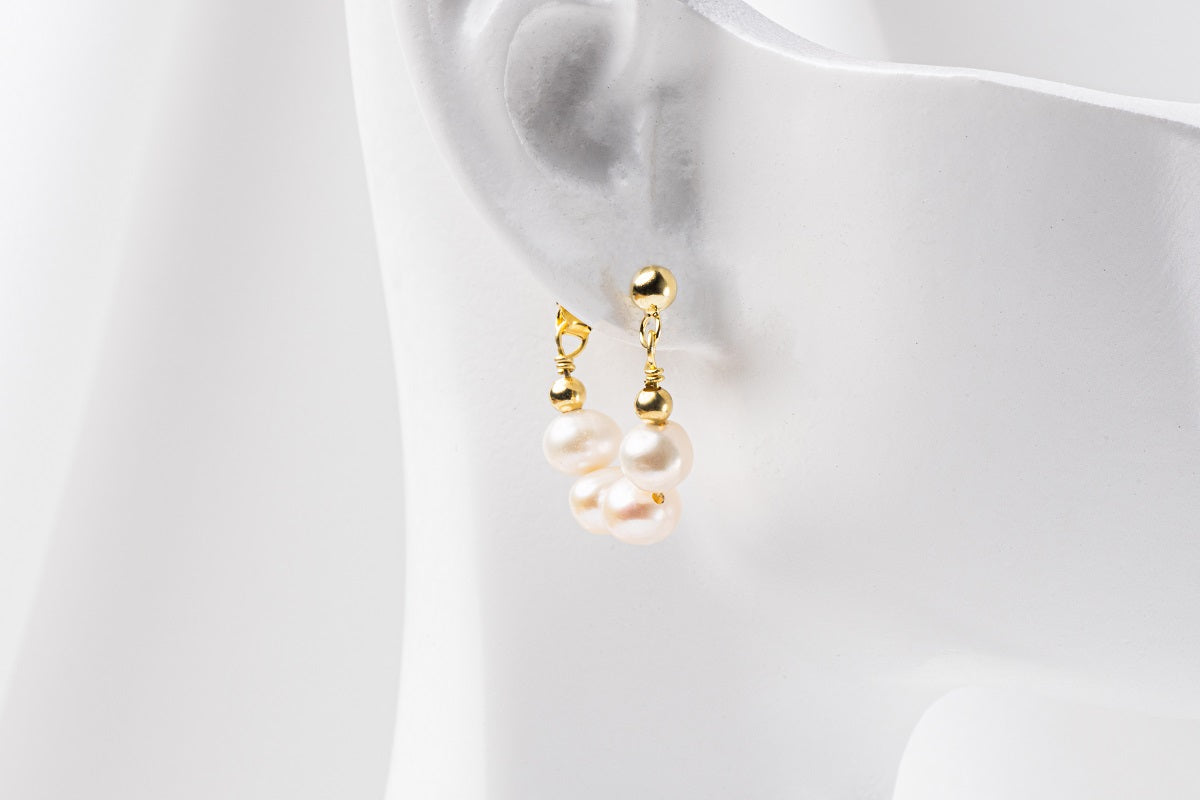 A pair of semi-dangle pearl earrings, made of sterling silver 925 and white color mini baroque-shaped pearls. On a white mannequine.