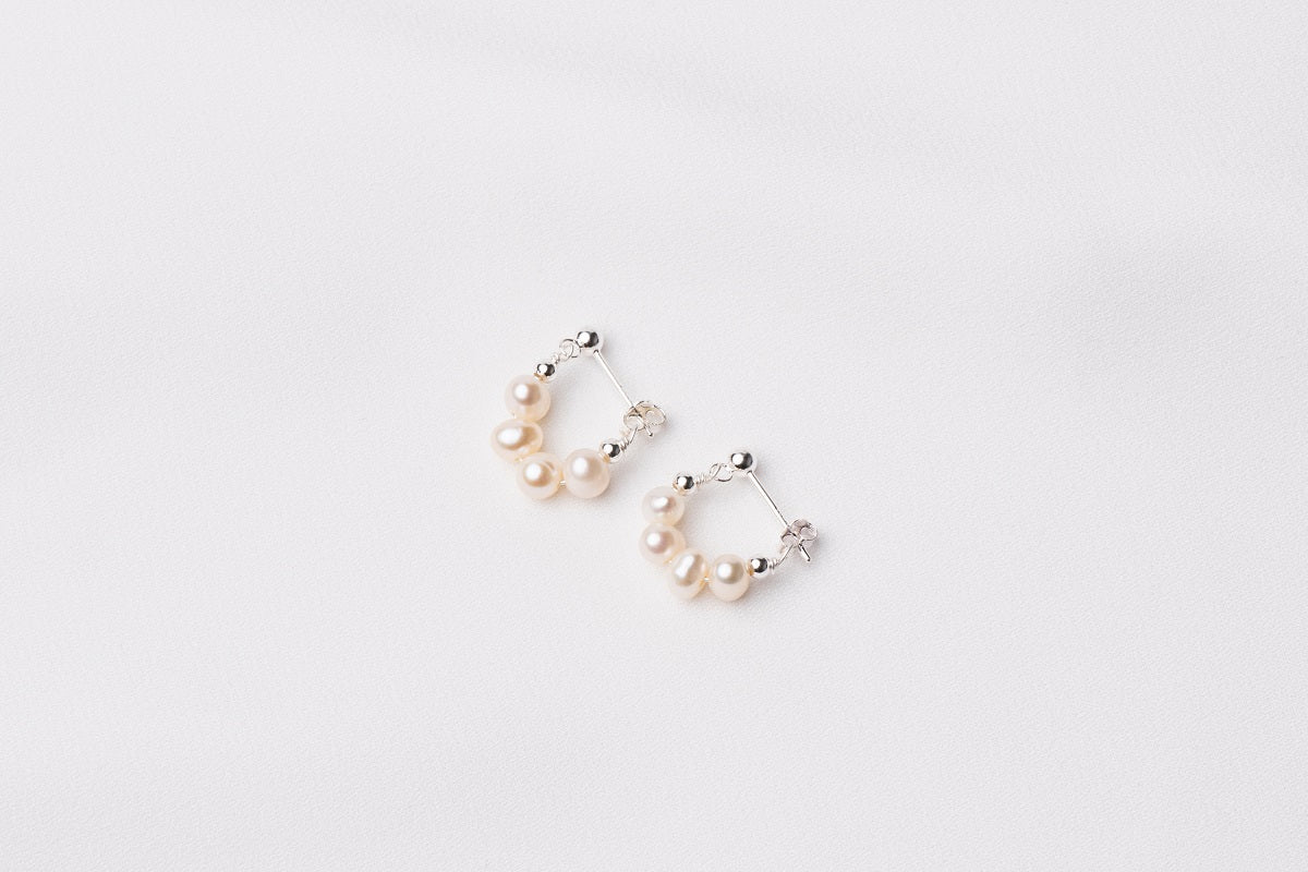 A pair of semi-dangle pearl earrings, made of sterling silver 925 and white color mini baroque-shaped pearls. On a white background.