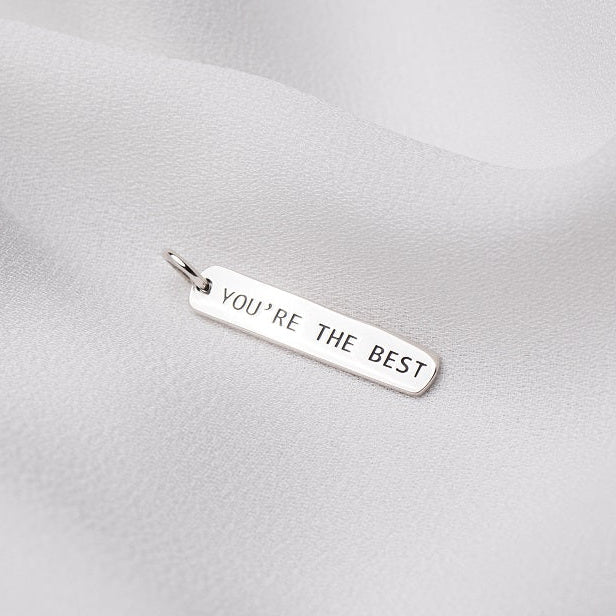 Silver pendant with "you're the best" engraved on it. On a white cloth background