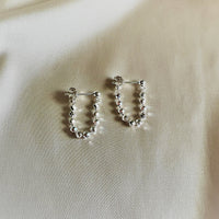 you and me silver earrings on a beige background 
